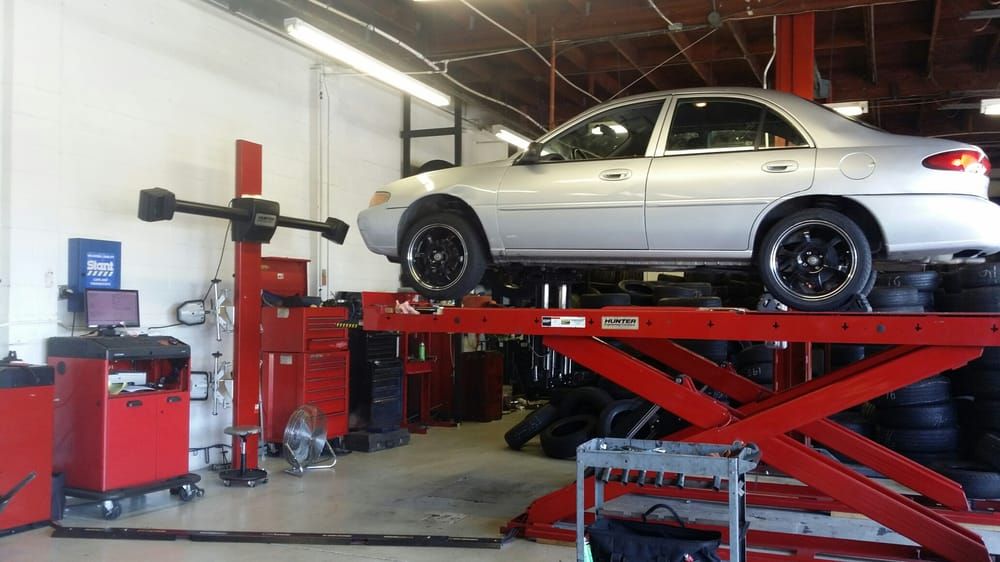 A silver sedan raised on a red alignment lift inside the shop